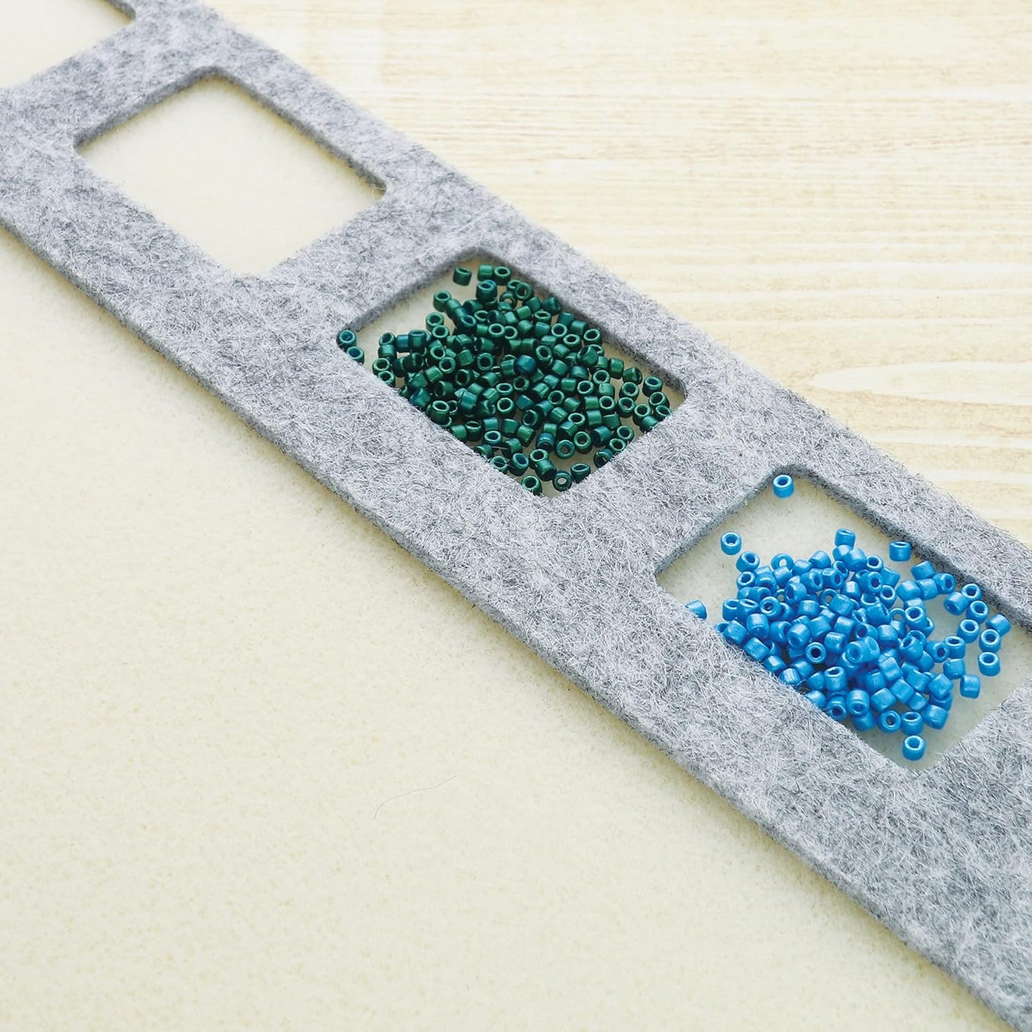 Seed beads in green and blue colors in a gray felt organizer.