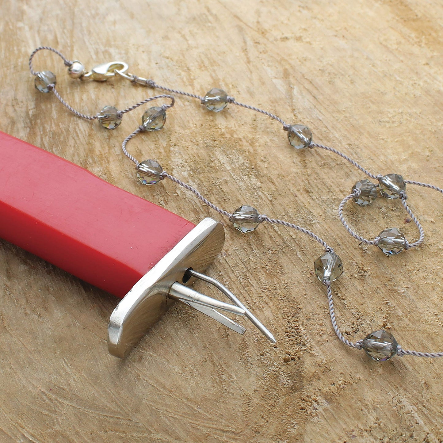 Gray beaded necklace with silver clasp next to a red wax carving tool.