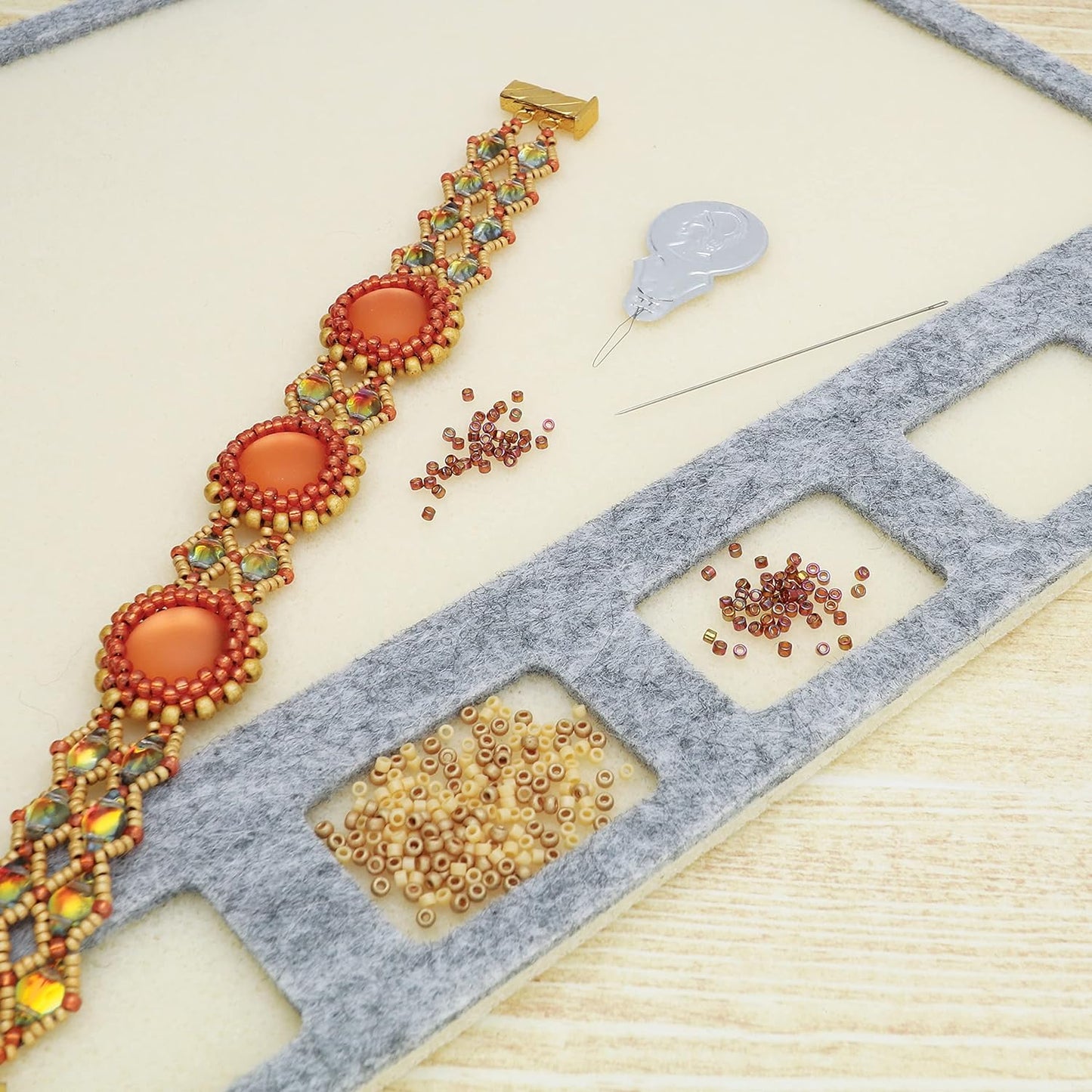 Handmade beaded bracelet with orange stones, seed beads, needle, and bead organizer tray.