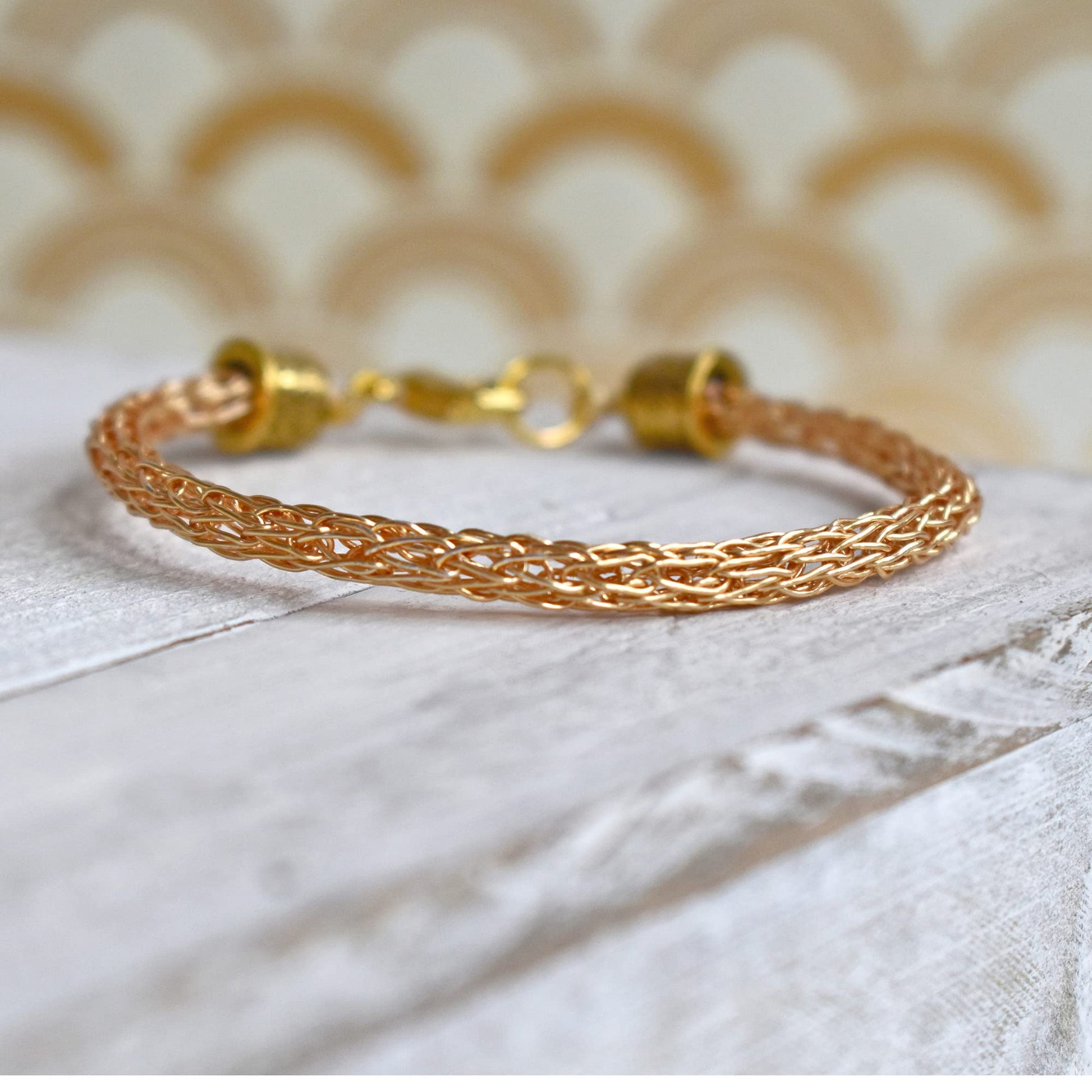 Close up of a gold woven chain bracelet with lobster clasp on a white wooden surface.